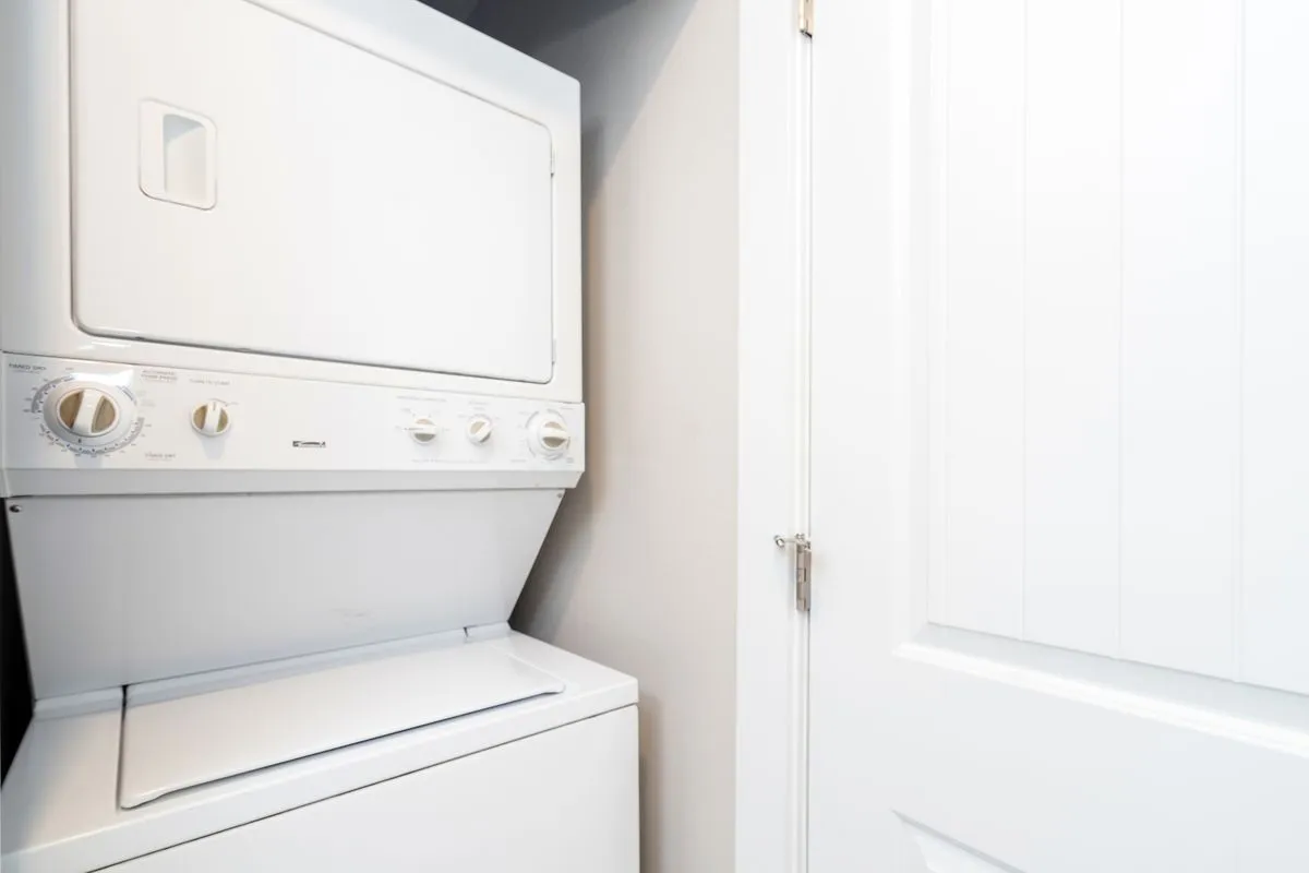 The image shows a stacked washer and dryer unit tucked neatly behind a white door, conveying an efficient, practical laundry area within the home.
