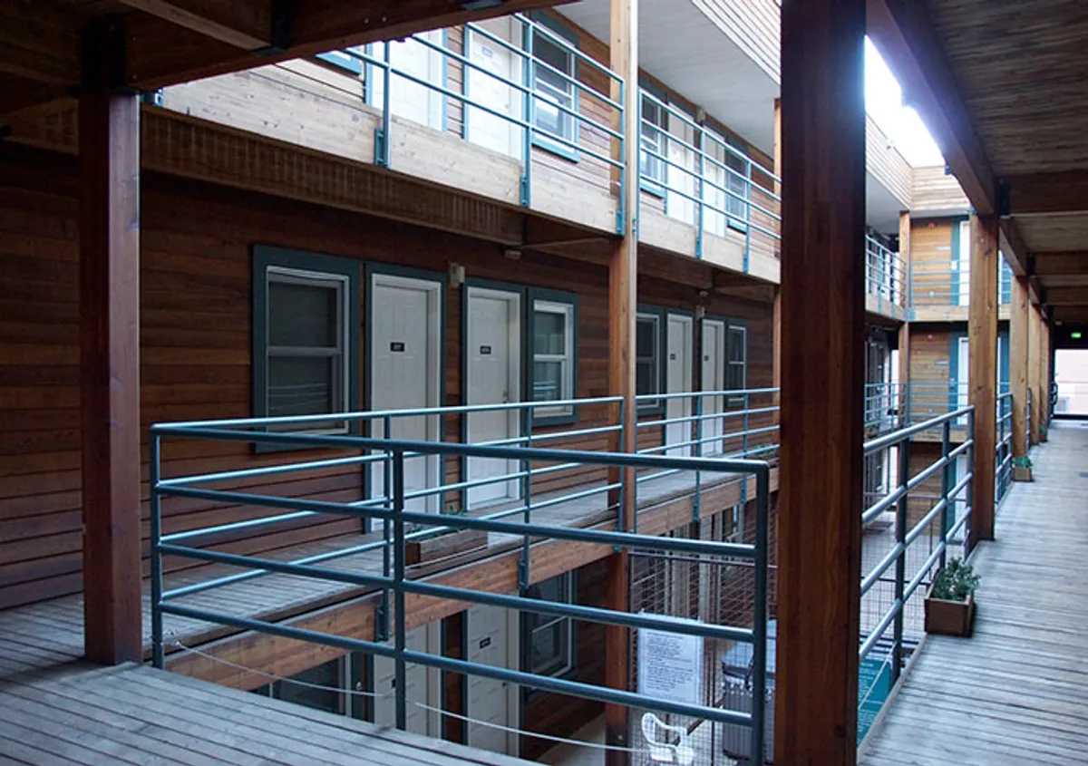 A welcoming balcony corridor with wooden railings, numbered doors, and planters brimming with greenery. The space feels communal and inviting, ideal for casual morning coffees or evening gatherings while taking in mountain air.