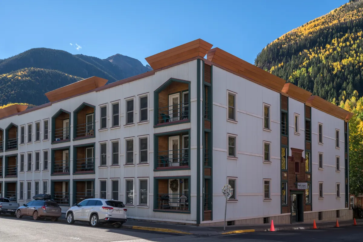 A contemporary building set against stunning mountain scenery, with balconies overlooking colorful autumn foliage. The scene radiates the energy of a vibrant community nestled in nature, with hiking trails and local shops easily accessible nearby.