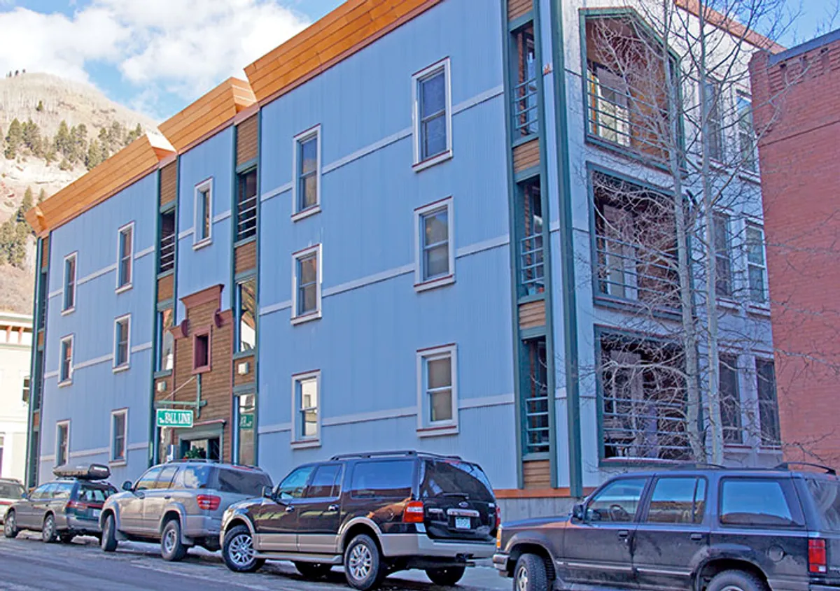 This exterior image displays the building's modern facade, welcoming entrance, and wooden architectural accents, suggesting secure, covered parking and elevator access within a contemporary, urban-mountain context.