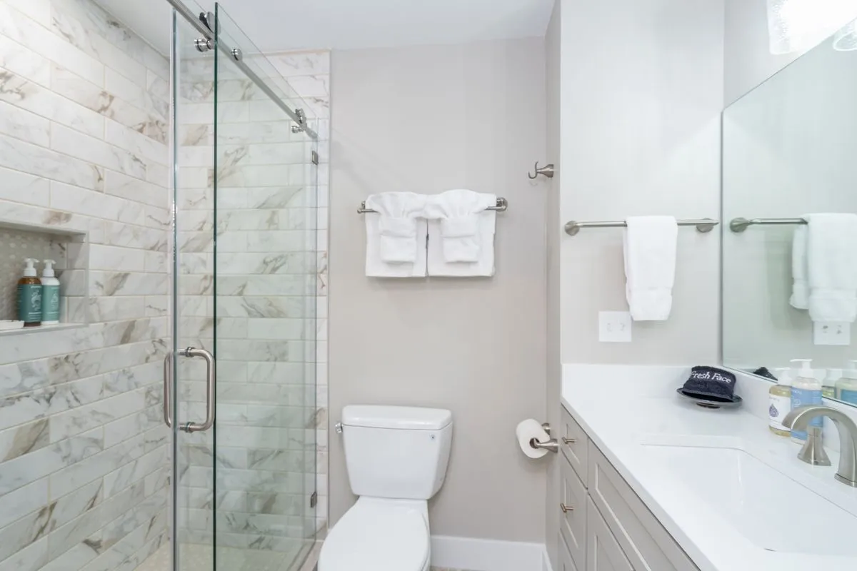 A modern bathroom with a glass shower enclosure, sleek marble tiles, a vanity with a sink, and neatly arranged towels. The clean lines and bright lighting give a sense of luxury and rejuvenation, perfect for refreshing after outdoor adventures.